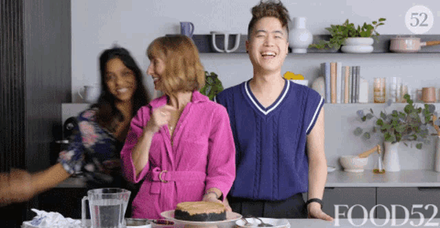 a woman in a pink robe is standing next to a man holding a cake in a kitchen with the words food52 on the bottom