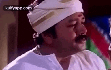 a man with a mustache is wearing a white turban and a white shirt .