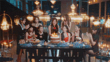 a group of women are sitting around a table with a cake on it