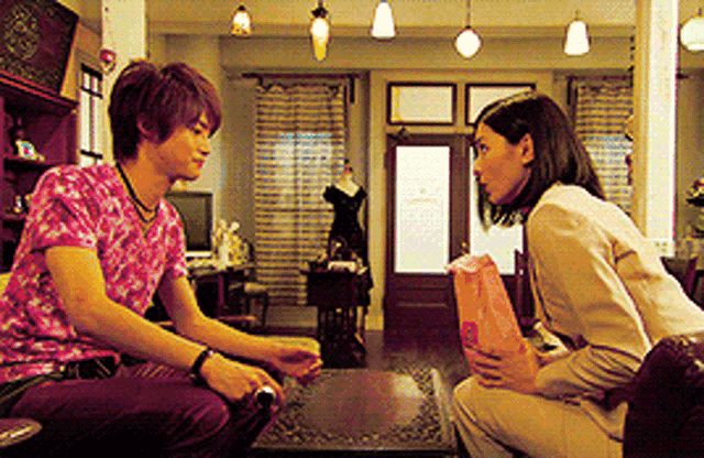 a man in a pink shirt sits next to a woman in a beige suit