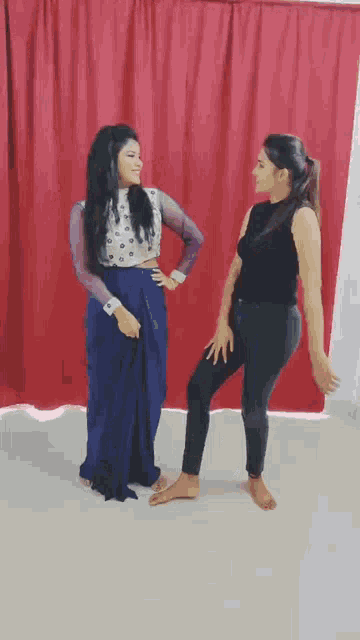 two women are standing next to each other in front of a red curtain ..