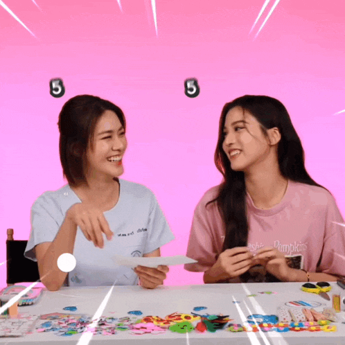 two women are sitting at a table with a pink background and a number 5 above them