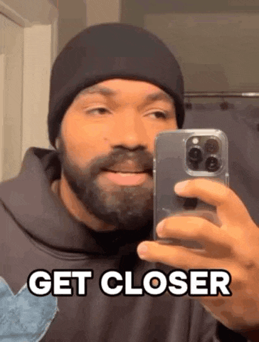 a man with a beard is taking a selfie in front of a mirror with his phone .