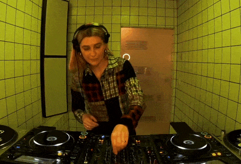 a woman wearing headphones and a plaid shirt is playing music on a turntable