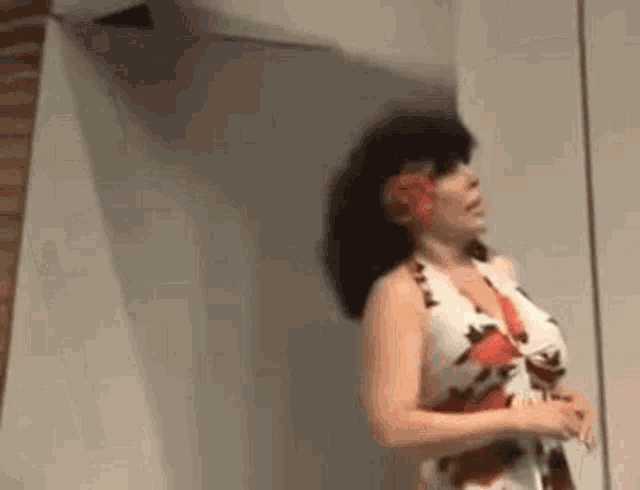a woman in a dress with a flower in her hair is standing in front of a white wall .