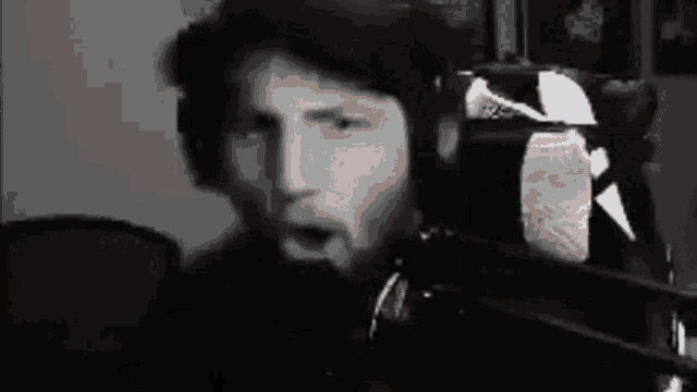 a black and white photo of a man sitting in front of a microphone with his mouth open .