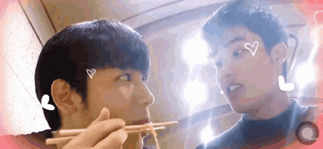 two men are eating noodles with chopsticks and hearts on their faces .