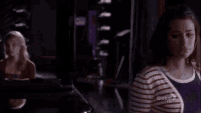 two women are standing next to each other in a dark room and one of them is wearing a striped shirt .