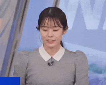 a woman in a gray sweater and white collar is standing in front of a microphone .