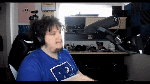 a man wearing headphones and a blue shirt is sitting in front of a microphone with the numbers 1 and 1 on it