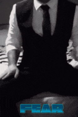 a man in a suit and tie is sitting on a bed with the word fear written in blue