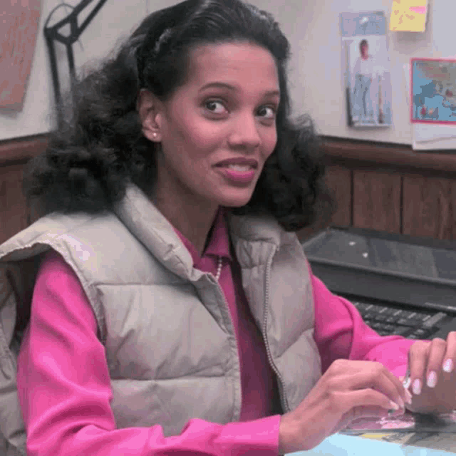 a woman wearing a pink shirt and a tan vest is sitting at a desk