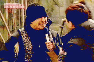 a man in a black hat is holding a microphone while talking to another man in a black jacket