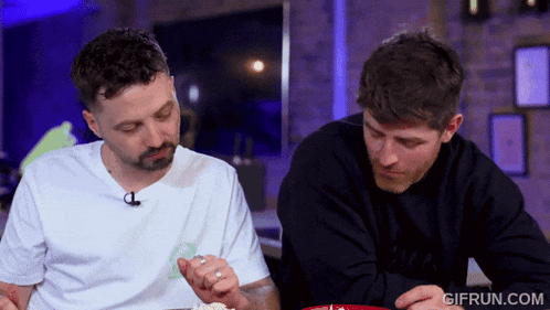 two men are sitting at a table with gifrun.com written on the bottom right