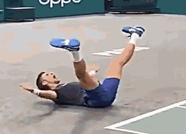 a man is laying on the ground on a tennis court with his legs up .