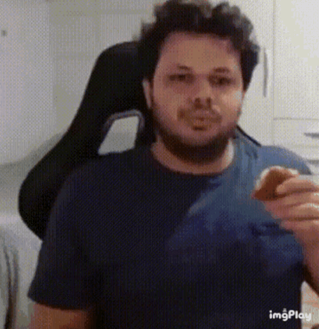 a man with a beard is sitting in a chair and eating a hamburger .