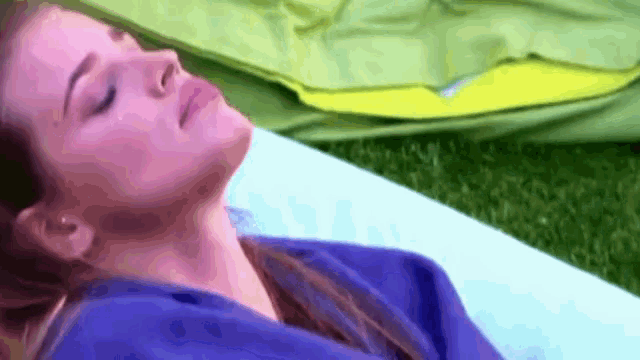 a woman in a blue shirt is laying on a blue blanket on the grass .