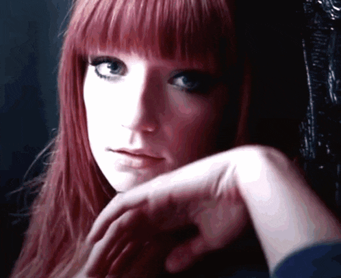 a woman with red hair has her hand on her chin