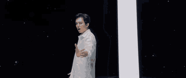 a man in a white shirt is standing in front of a white light and pointing .