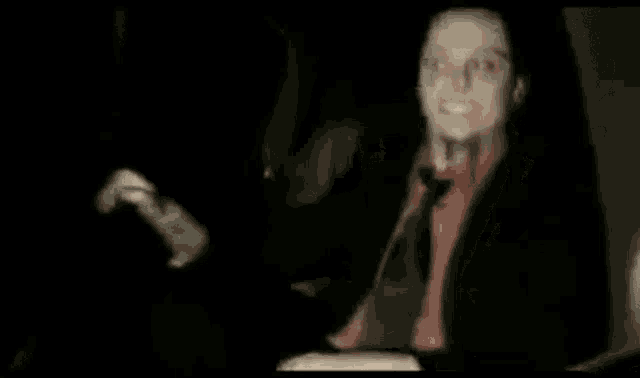 a man in a suit and tie is sitting in a dark room .