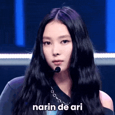 a woman with long black hair is wearing a microphone and says narn de ari in white letters