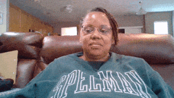 a woman wearing glasses and a green spellman sweatshirt