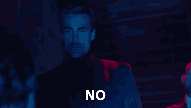 a man in a suit stands in a dark room and says no