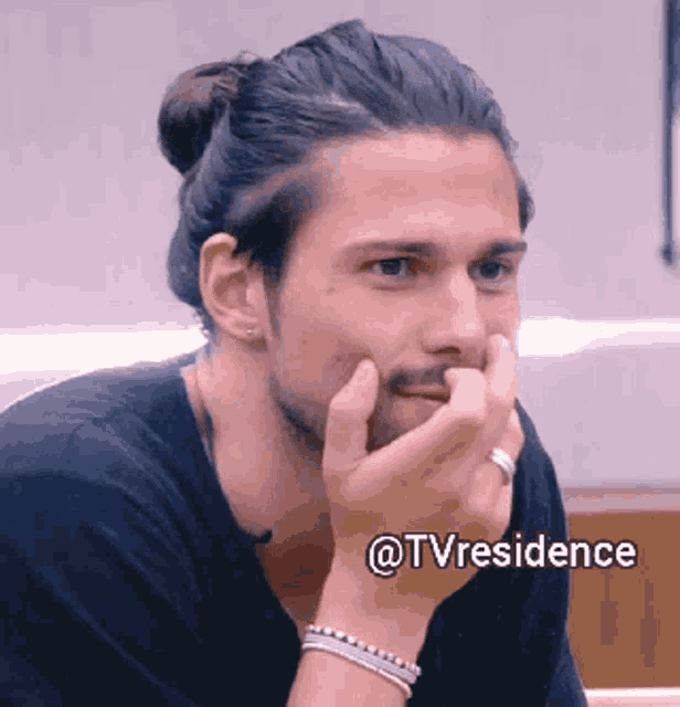 a man with long hair and a beard is sitting with his hand on his chin and the words @tvresidence below him