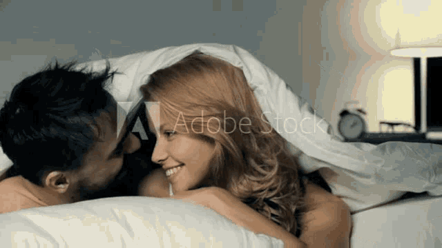 a man and a woman are kissing under a blanket with adobe stock in the background