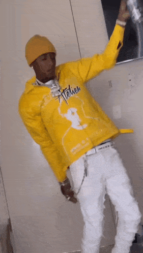 a man in a yellow jacket and white pants is standing in a room holding a can of soda .