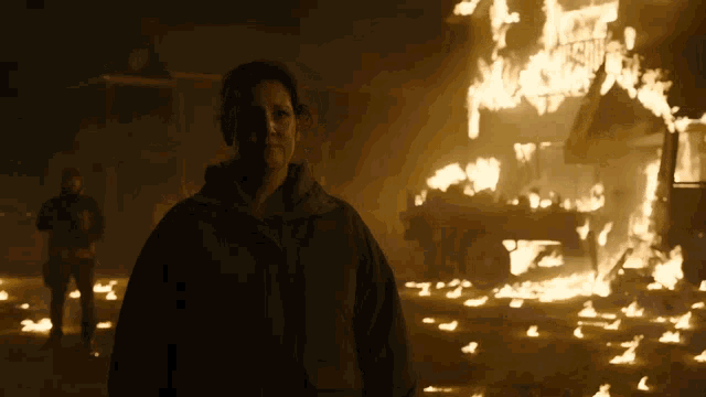 a man in a black jacket stands in front of a burning building with a sign that says ' justice ' on it