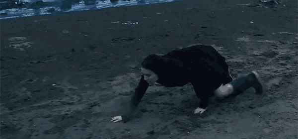 a woman in a black coat is kneeling on a beach