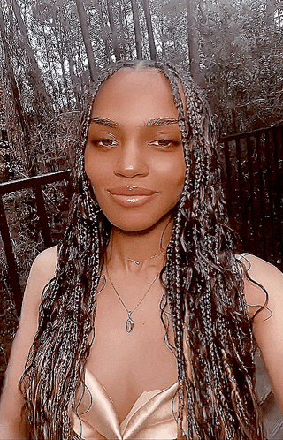 a woman with braids is wearing a gold top and a necklace with the letter o on it
