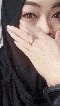 a woman wearing a ring on her finger covering her mouth