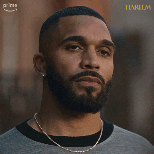 a man with a beard is wearing a grey shirt and a gold chain around his neck and says alright