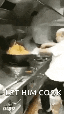 a man is standing in a kitchen cooking food in a large wok .