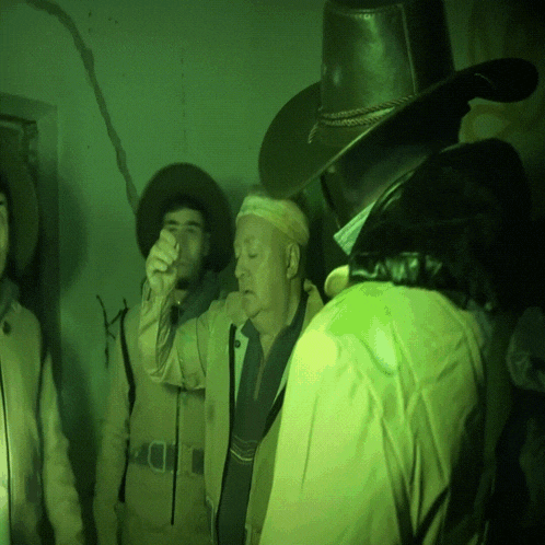 a man wearing a cowboy hat stands in a dark room