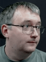 a man wearing glasses and a grey shirt is making a funny face .