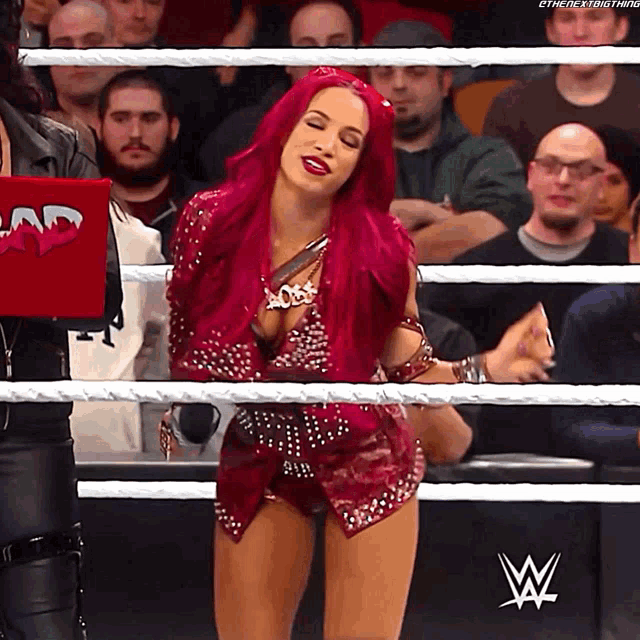 a woman with red hair is in a wrestling ring with a w logo on the wall behind her