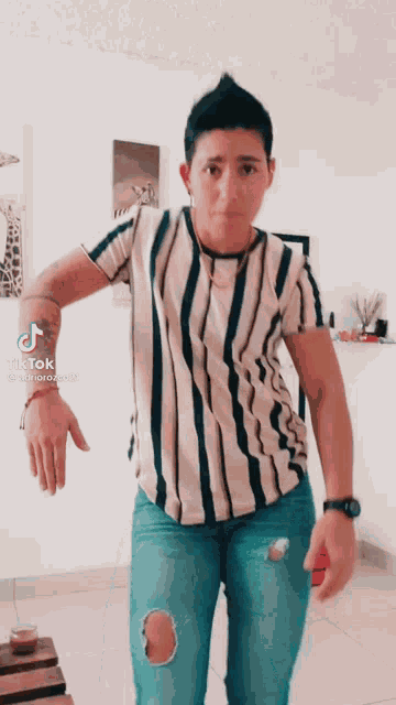 a woman wearing a striped shirt and ripped jeans is standing in a living room ..
