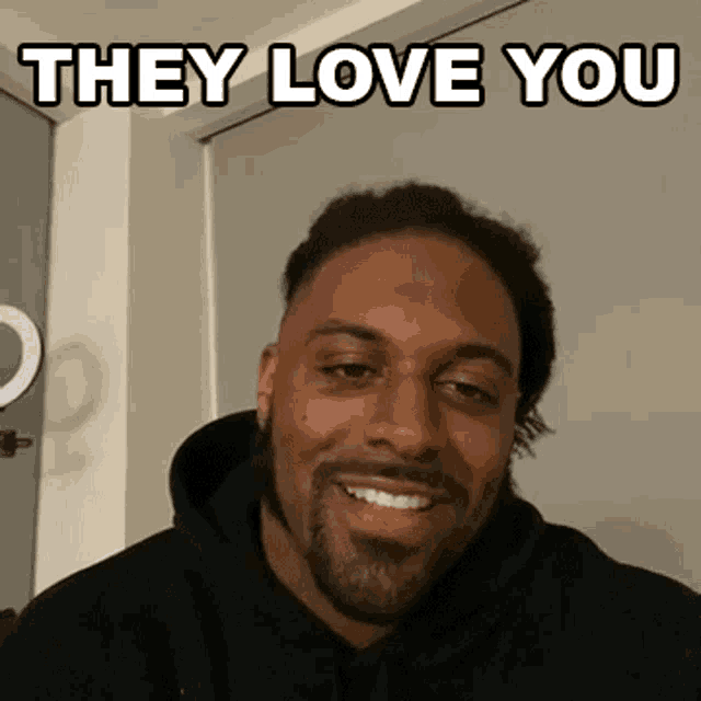 a man in a black hoodie smiles with the words they love you above him