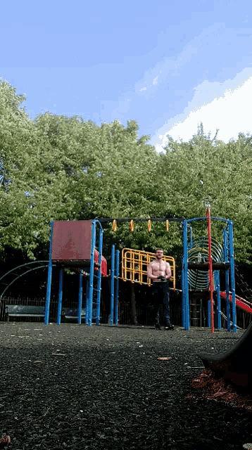 a shirtless man is standing in a playground with a blue slide