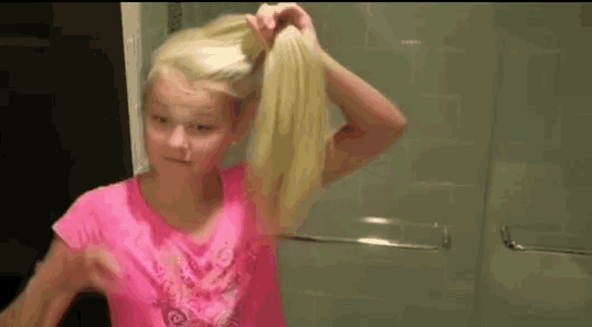 a young girl in a pink shirt is tying her hair in a ponytail .