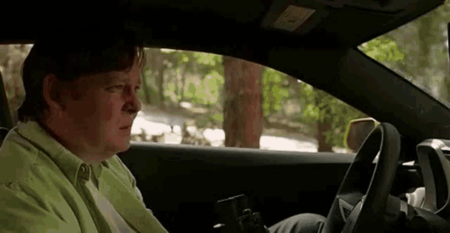 a man in a green shirt is sitting in a car with a camera .