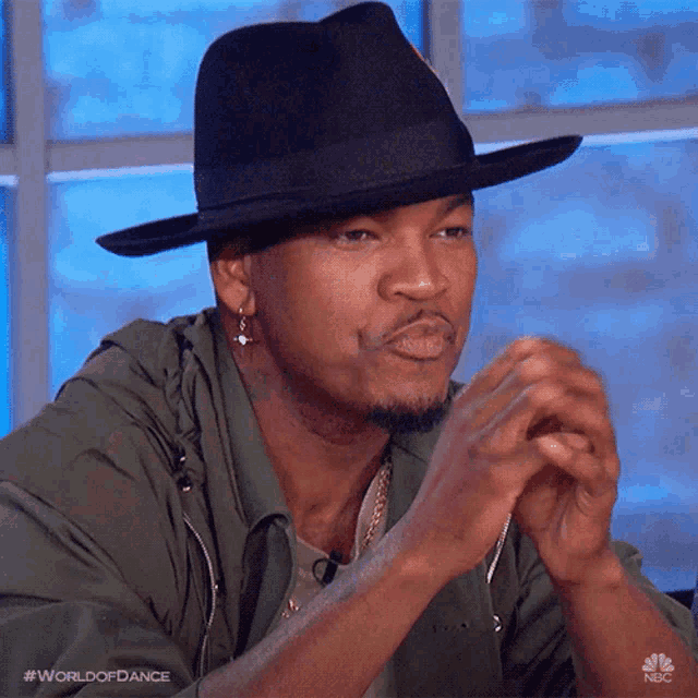 a man wearing a black hat is sitting in front of a window with the words world of dance on the bottom