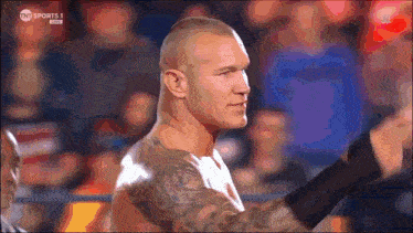 a man with a tattoo on his arm is standing in front of a crowd with tnt sports 1 on the screen