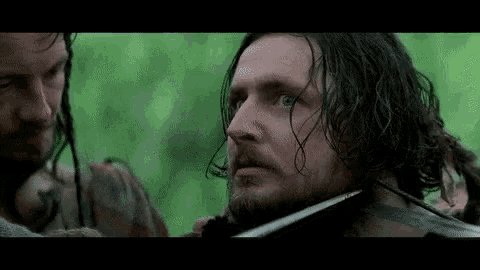 a man with long hair and a beard is holding a sword in his mouth in a movie .