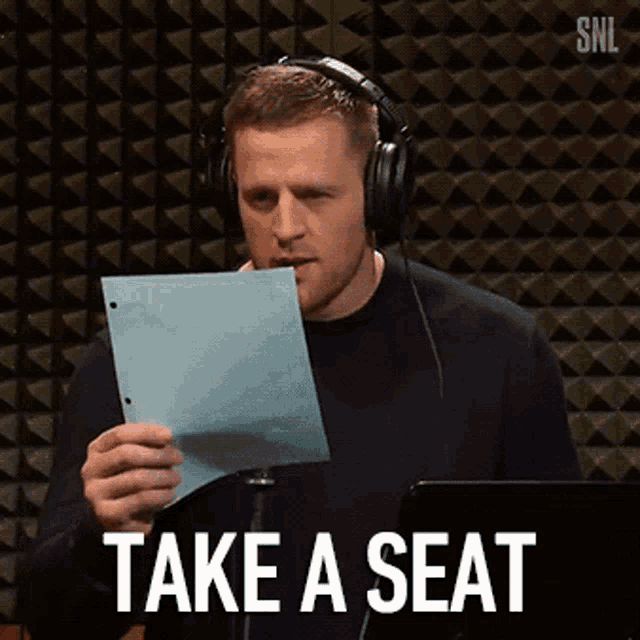 a man wearing headphones is holding a piece of paper with the words take a seat written on it .