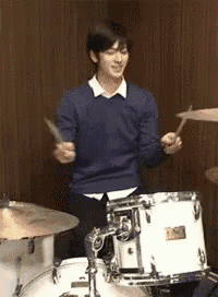 a man in a blue sweater is playing a drum set