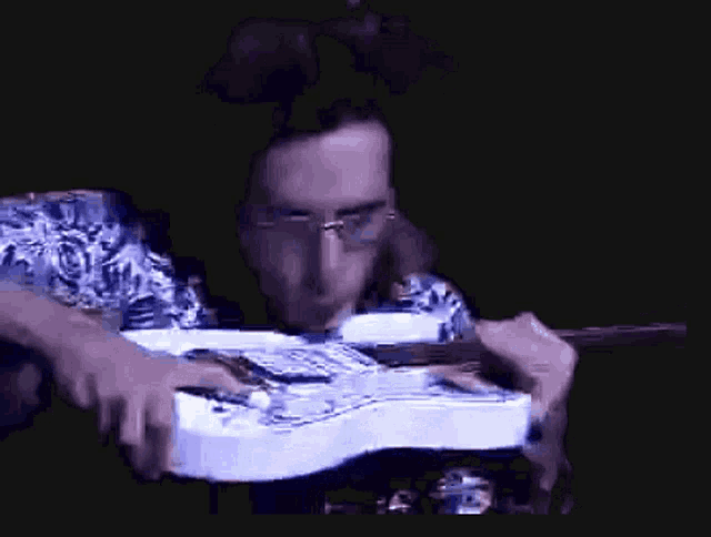 a man wearing glasses is playing a white electric guitar